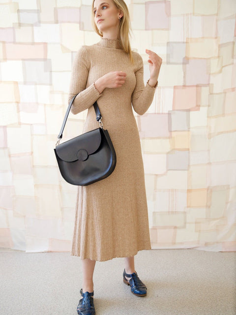 2. Woman wearing TOKS VISOKS FIONA Handbag in black, paired with a beige dress, highlighting adjustable strap