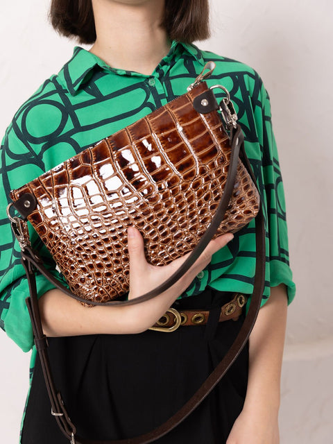 1. Woman holding TOKS VISOKS TOMMY leather bag with alligator pattern, styled with green patterned shirt