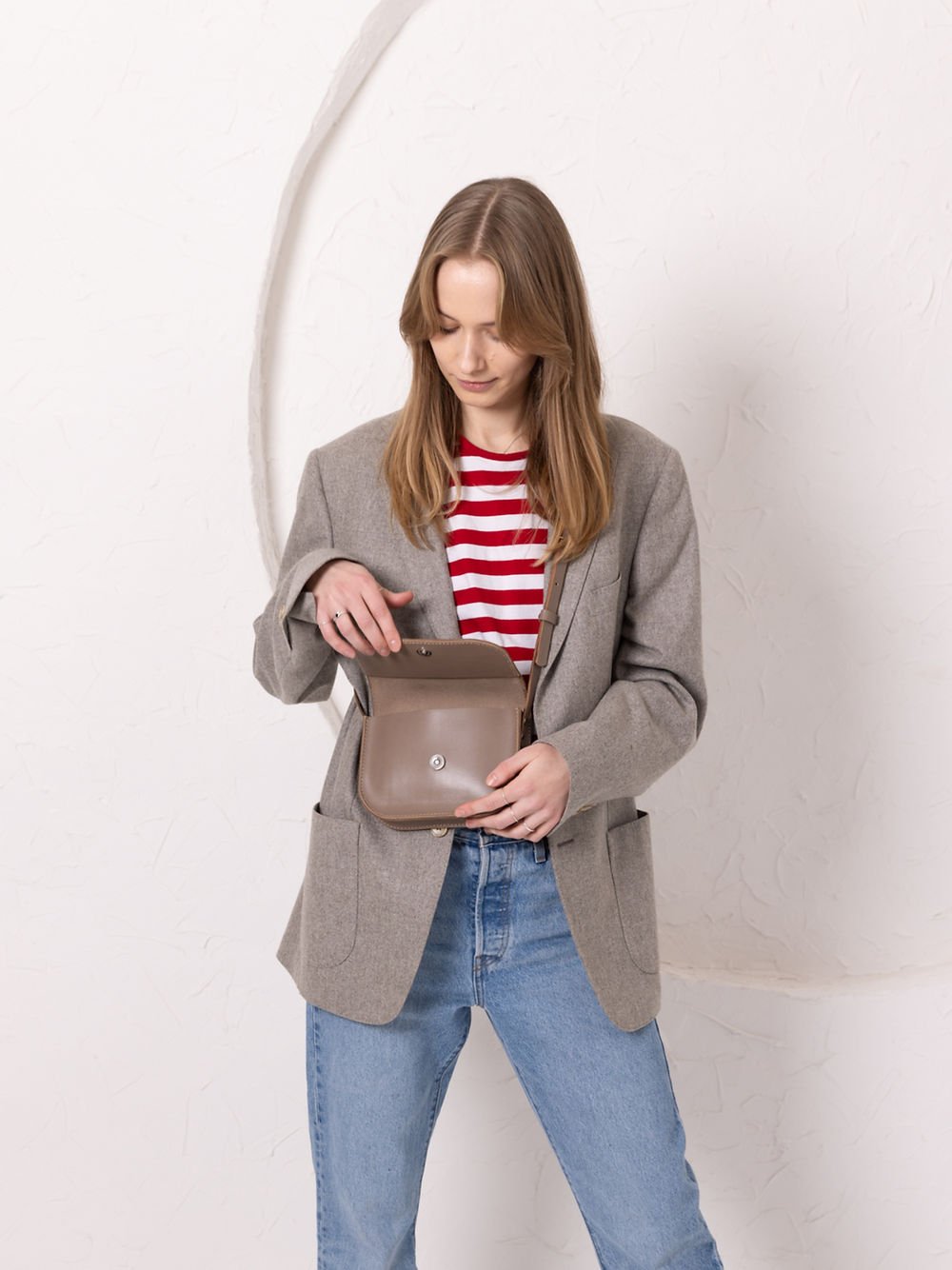 9. Woman opening TOKS VISOKS RUBY Purse in beige, showing interior and magnet buckle closure