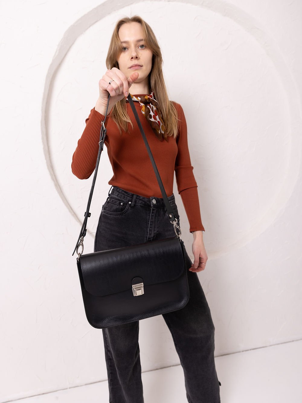 4. Woman showcasing TOKS VISOKS ASTORIA black leather handbag with adjustable strap and buckle