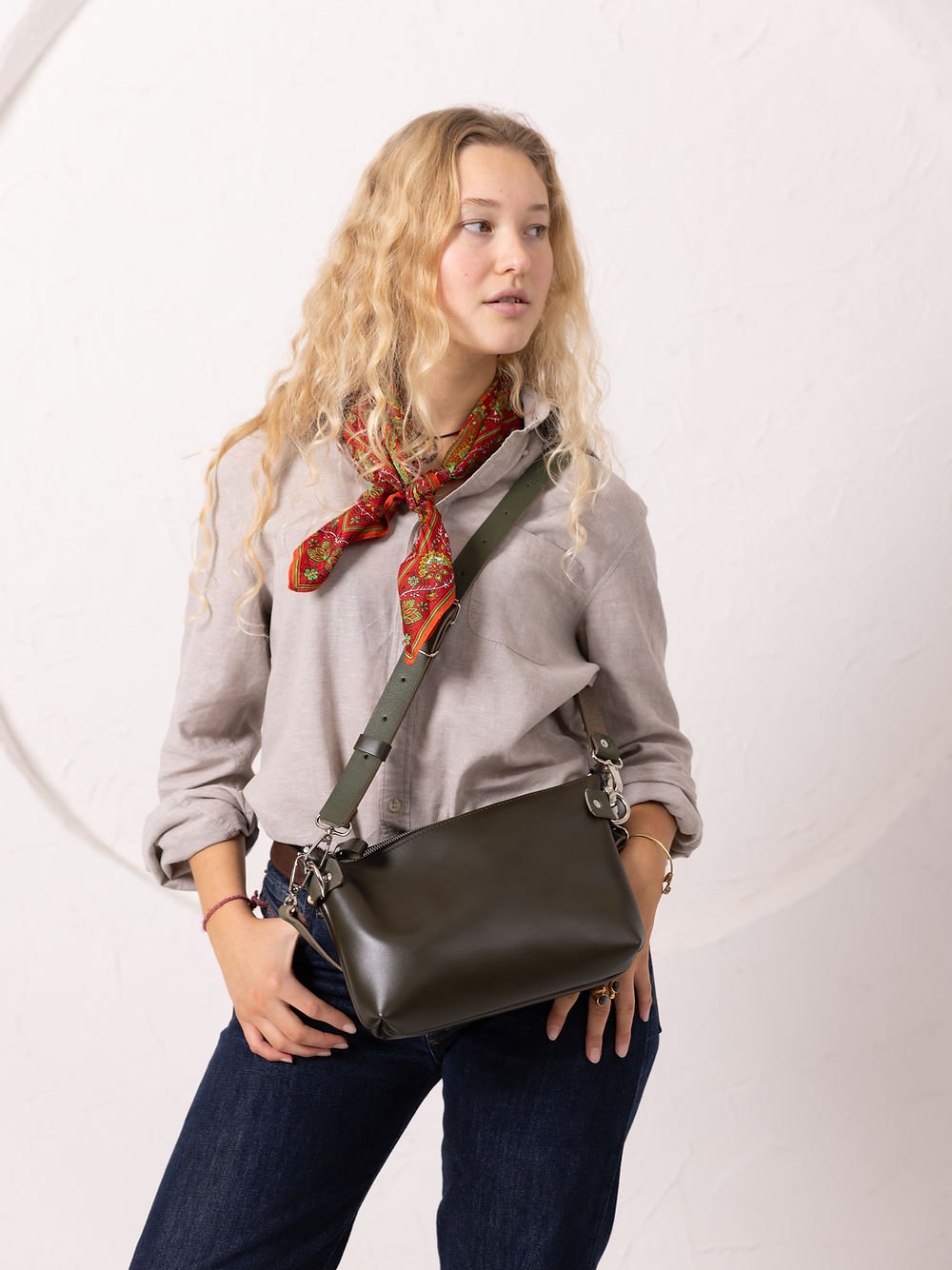 7. Women's TOMMY leather bag in dirty green worn crossbody, highlighting adjustable strap in studio setting
