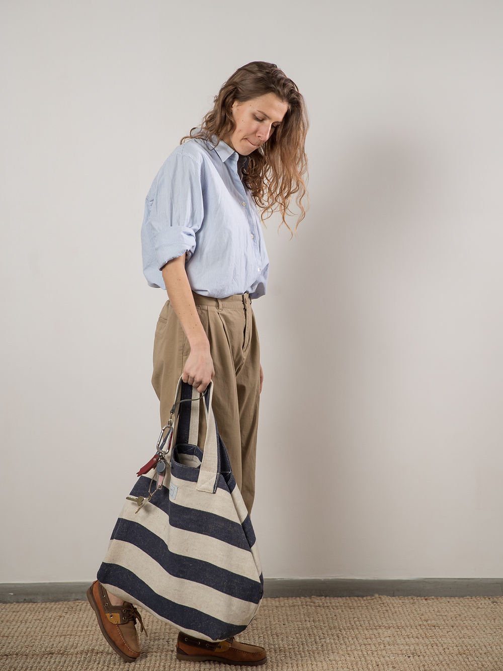 1. Woman carrying TOKS VISOKS oversized beach bag in reclaimed stripe canvas, shown in lifestyle setting