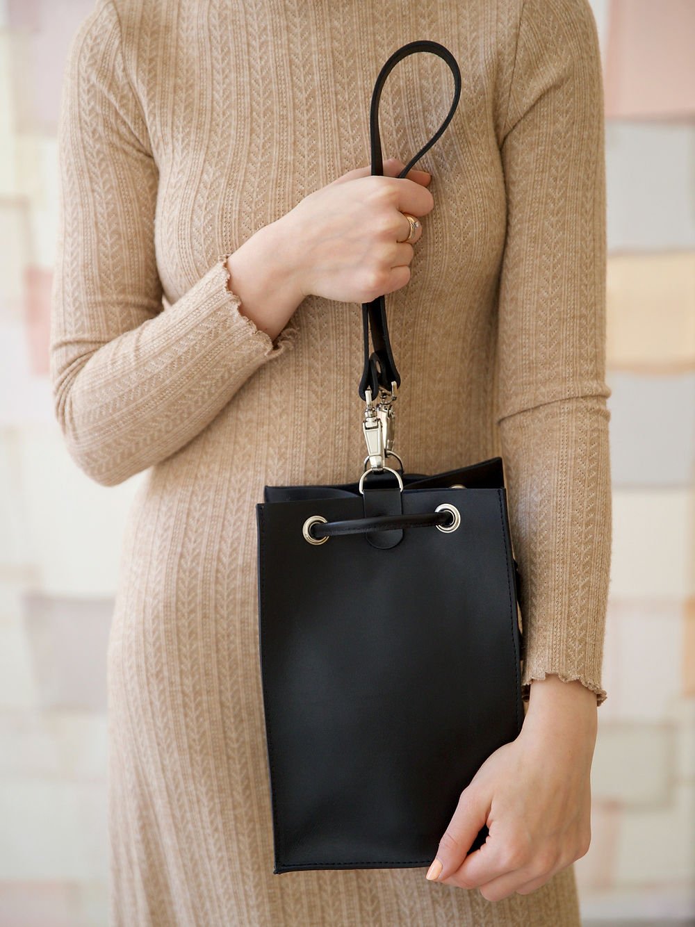6. Studio shot of woman holding black TOKS VISOKS PIPER Purse, emphasizing strap and closure