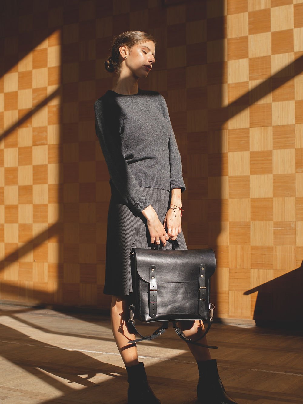 3. Woman holding black leather BENJAMIN Backpack by TOKS VISOKS, shown in a lifestyle setting