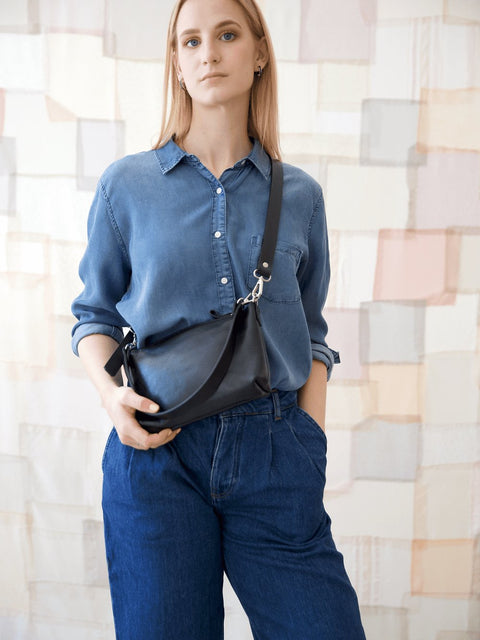 5. Women's black TOMMY leather bag by TOKS VISOKS worn crossbody, front view in lifestyle setting