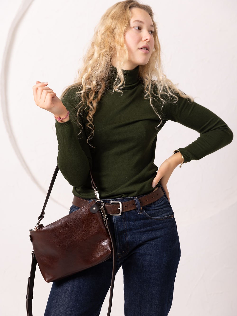 5. Woman posing with TOKS VISOKS TOMMY leather bag in cognac, styled with green turtleneck and jeans