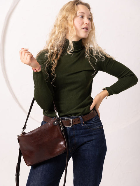 5. Woman posing with TOKS VISOKS TOMMY leather bag in cognac, styled with green turtleneck and jeans