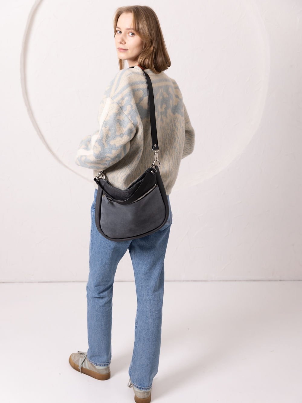 7. Woman showcasing TOKS VISOKS STELLA grey leather handbag with suede detail, styled in lifestyle setting