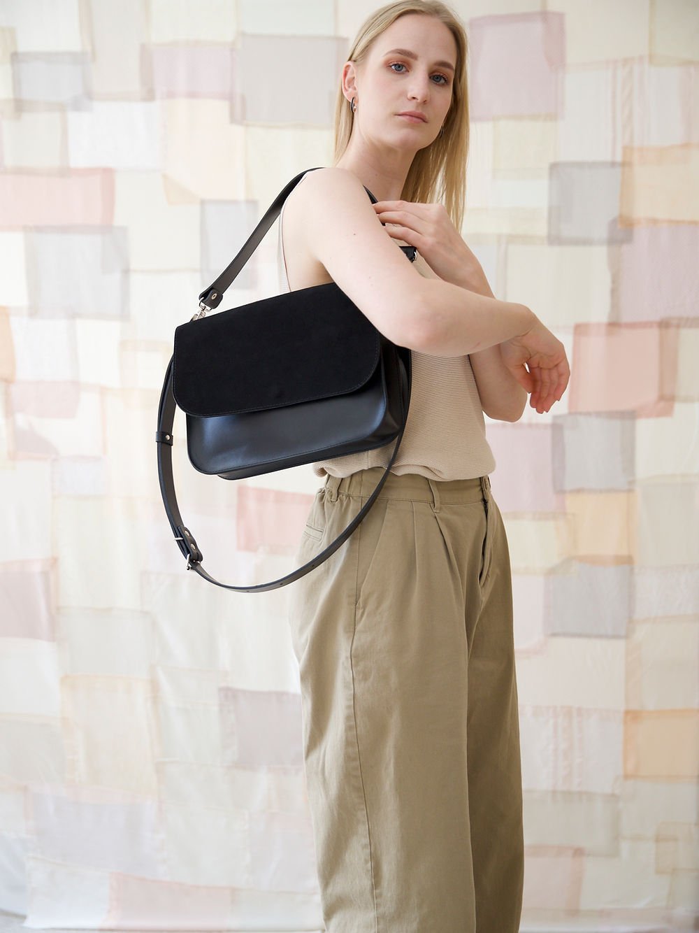 13. Woman wearing TOKS VISOKS ASTORIA black suede handbag crossbody, styled with beige top and khaki pants