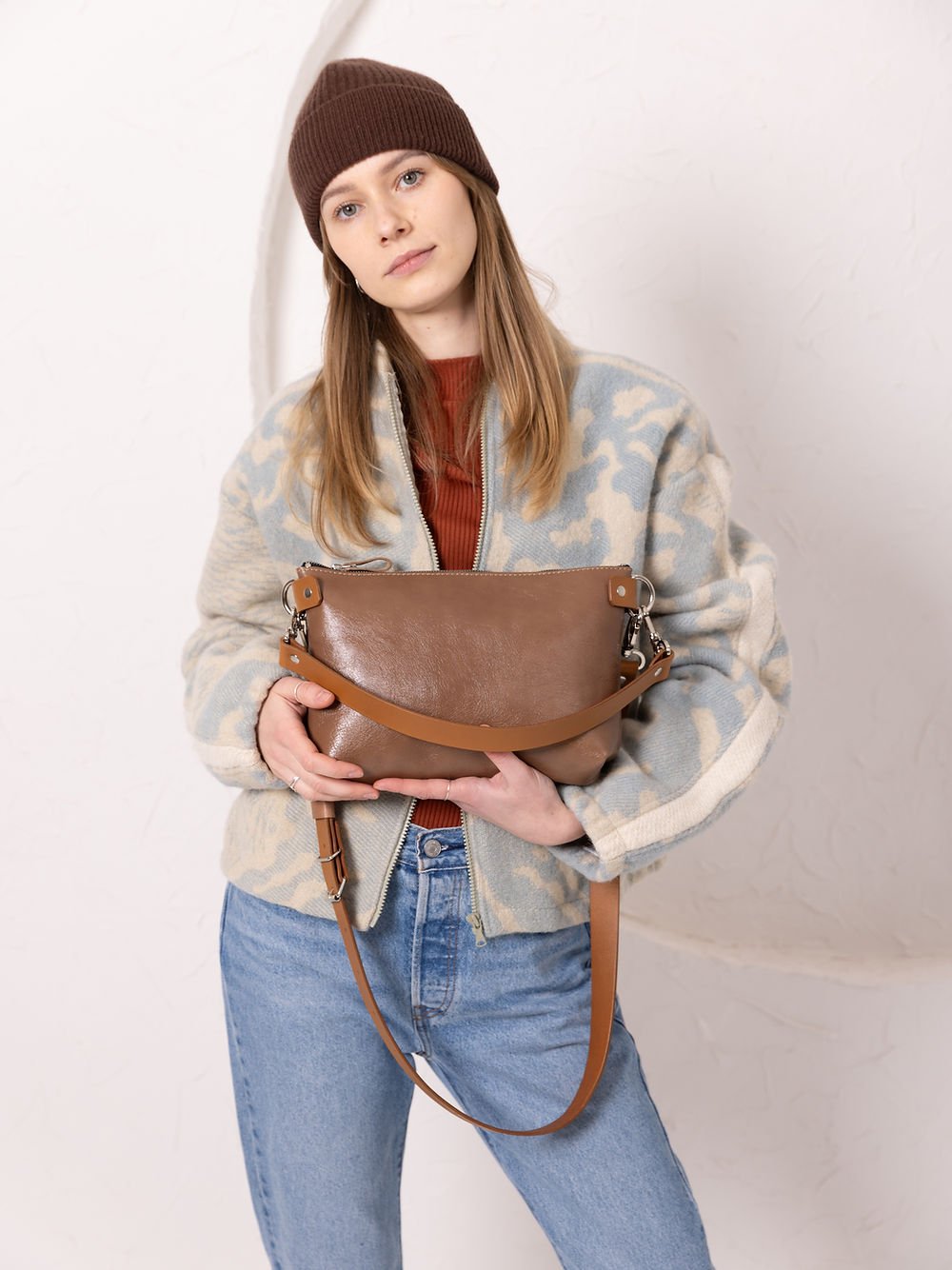 3. Woman holding TOKS VISOKS TOMMY leather bag in cappuccino, demonstrating clutch transformation