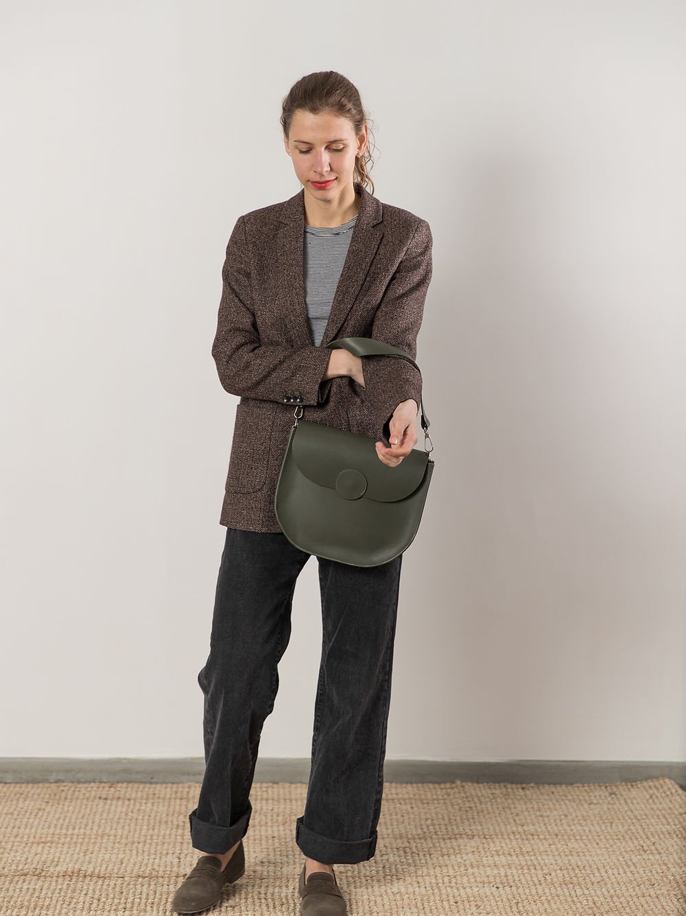 2. Woman holding TOKS VISOKS FIONA Handbag in faded green, styled with casual outfit in studio
