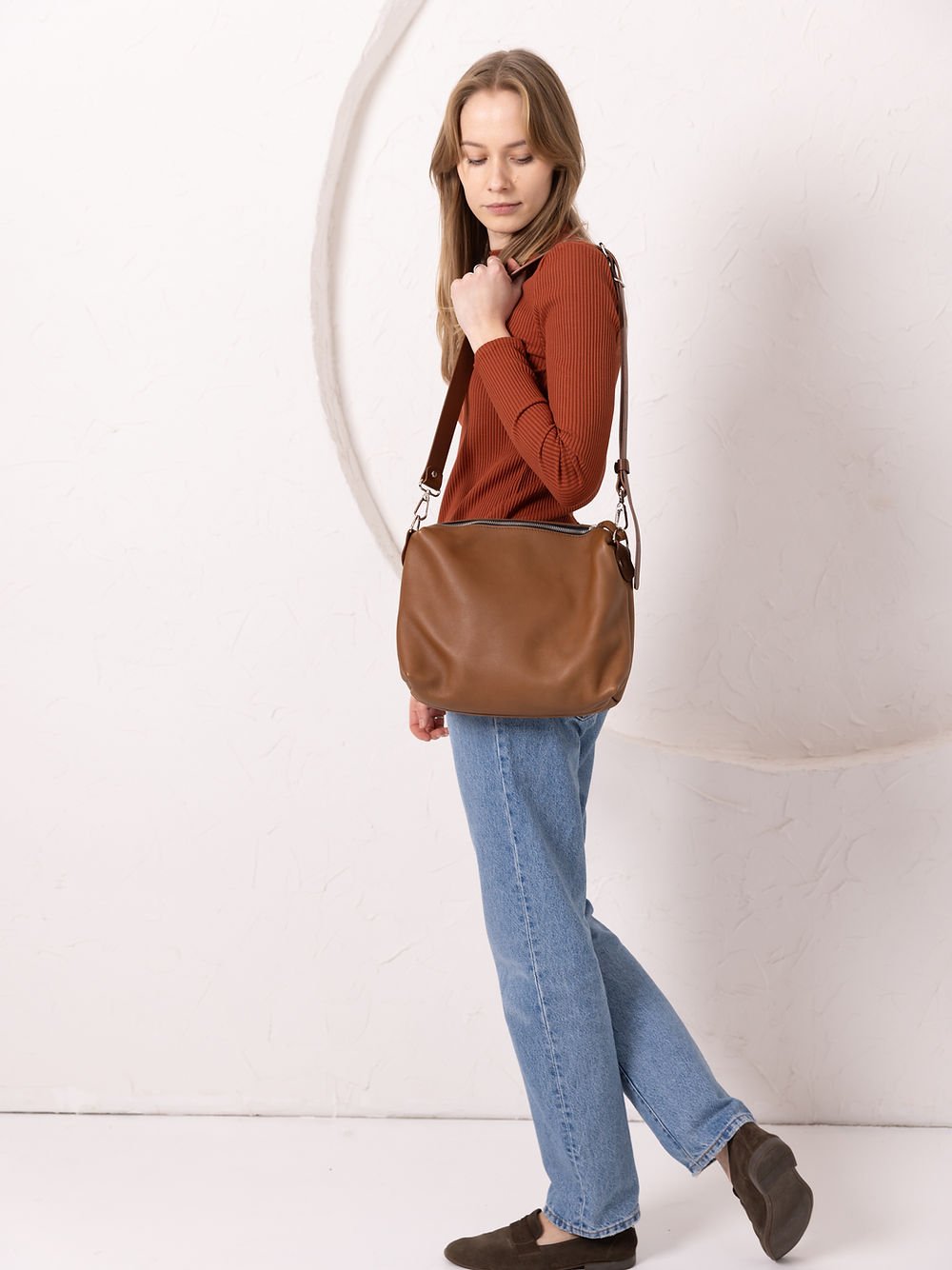 3. Woman showcasing TOKS VISOKS ROBIN leather handbag in camel brown, side view in studio