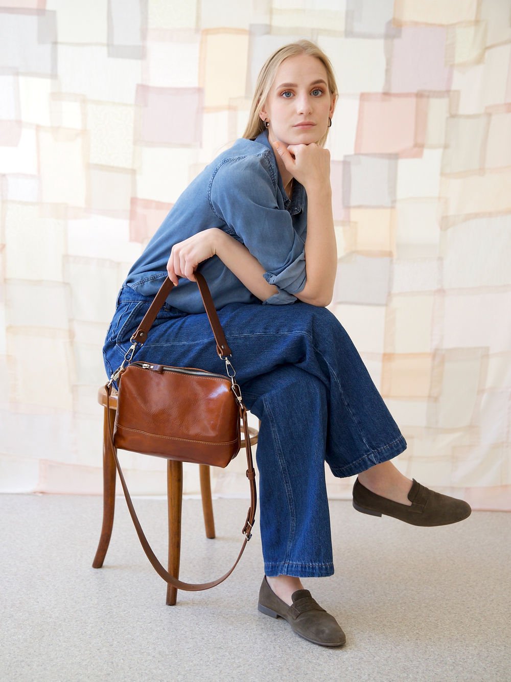 9. Woman sitting with TOKS VISOKS ROBIN leather handbag in ginger brown, styled with denim and loafers