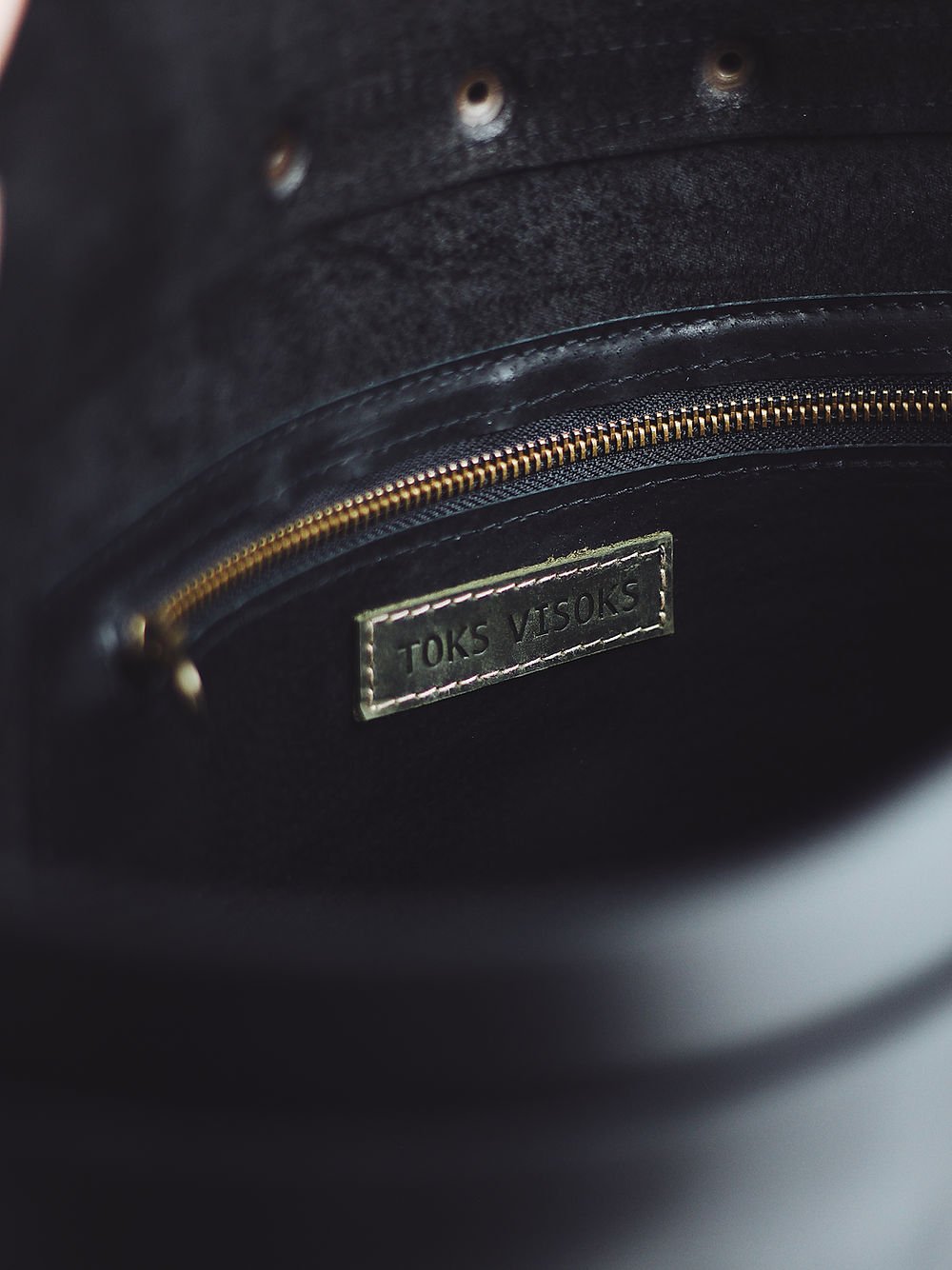 9. Interior view of black leather BENJAMIN Backpack by TOKS VISOKS, showing brand label and zip pocket