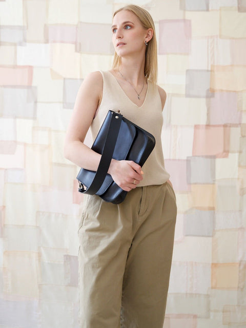 1. Woman holding TOKS VISOKS ASTORIA black handbag with short shoulder strap, styled for city life