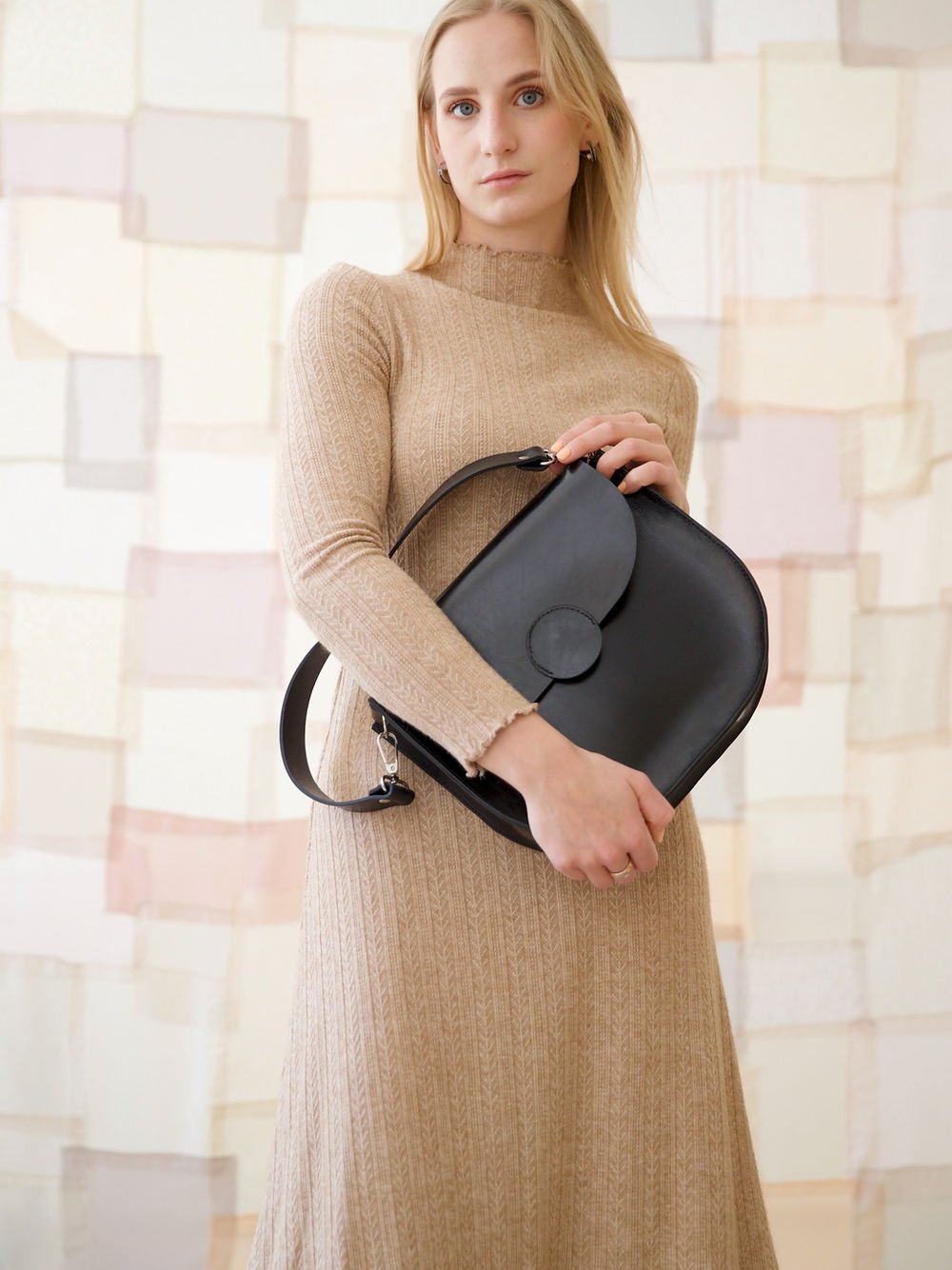 1. Woman holding TOKS VISOKS FIONA Handbag in black, styled with a beige dress, showcasing elegant design