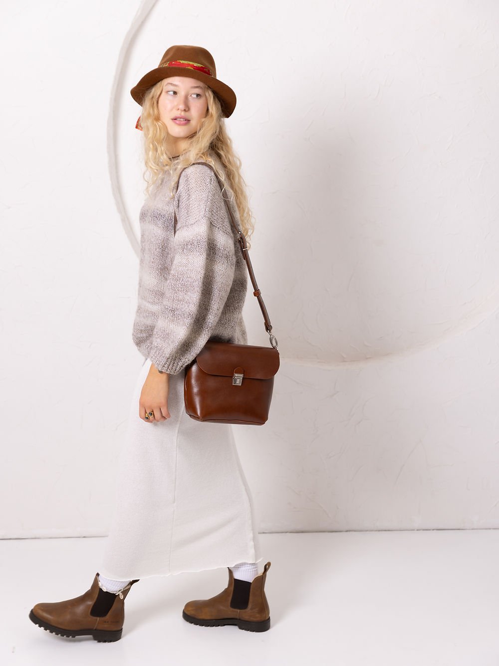 1. Woman wearing TOKS VISOKS ARLO Purse in ginger with adjustable strap, styled with a hat and casual outfit in lifestyle setting
