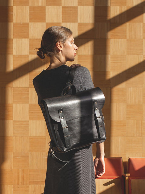 2. Woman carrying black leather BENJAMIN Backpack by TOKS VISOKS, shown from the back in a lifestyle setting