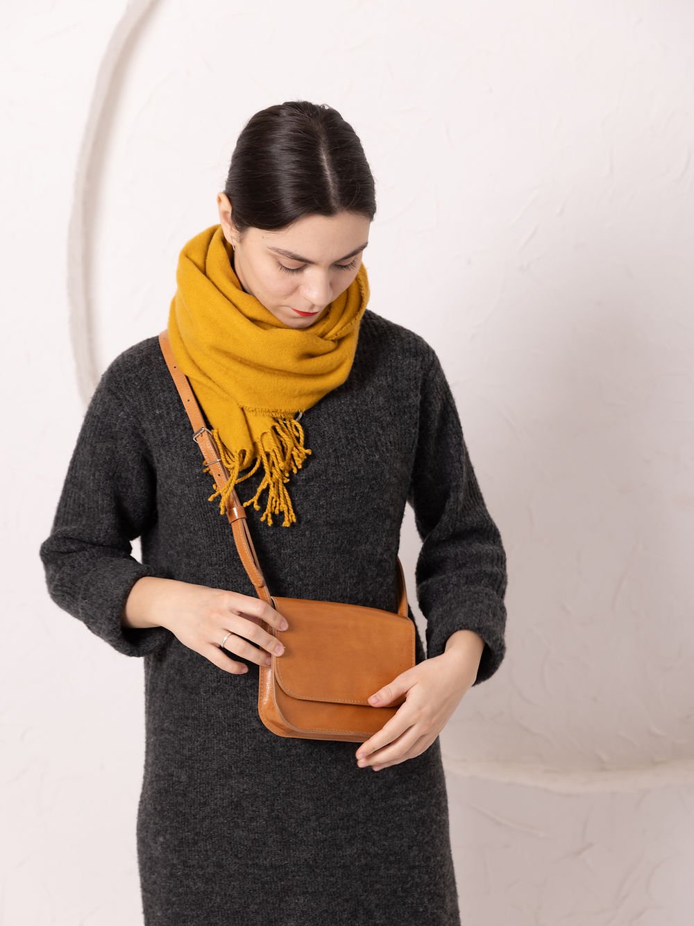 3. Woman wearing TOKS VISOKS RUBY Purse in caramel leather crossbody style, with yellow scarf and dark dress