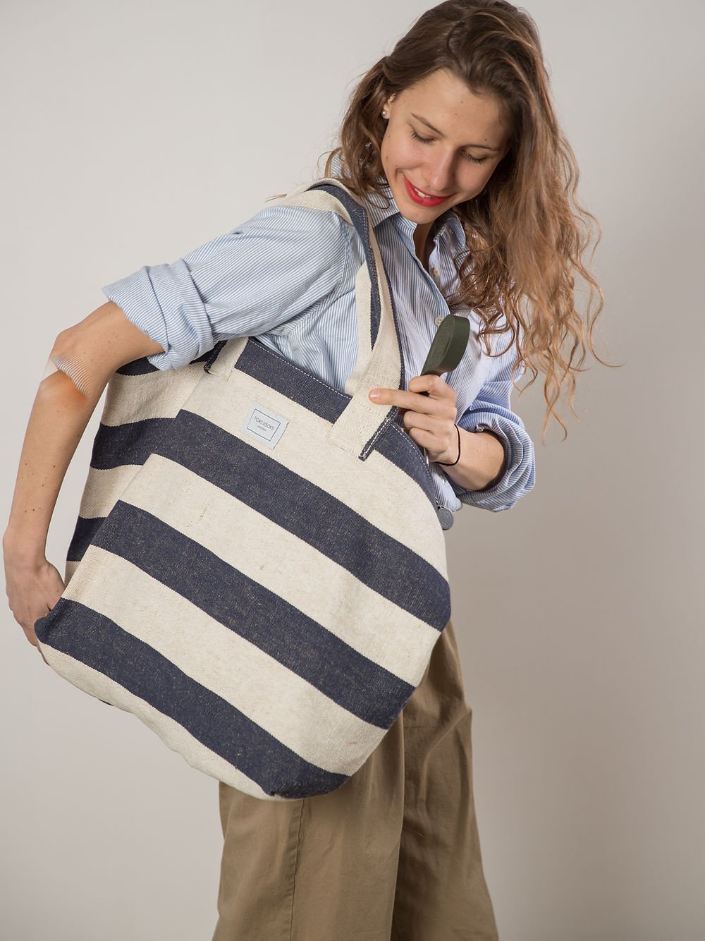 3. Woman smiling with TOKS VISOKS oversized beach bag in reclaimed stripe canvas, lifestyle image