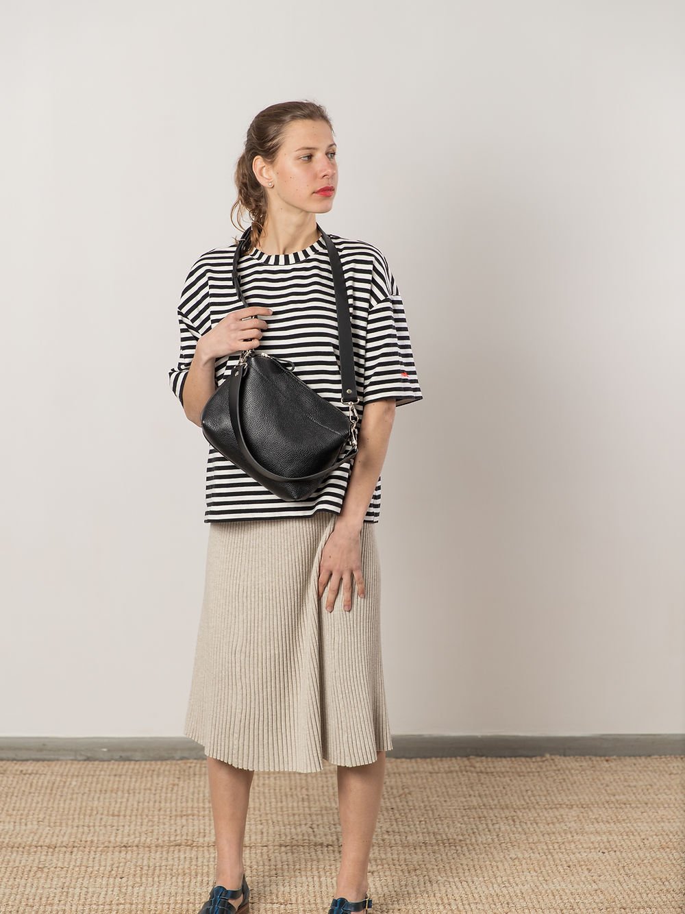 2. Woman wearing TOKS VISOKS ROBIN black leather handbag with two handles, styled with striped top and skirt