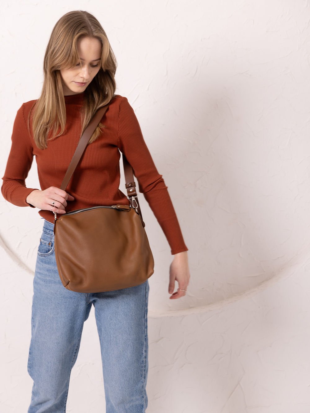 7. Woman displaying TOKS VISOKS ROBIN leather handbag in camel brown, front view in studio