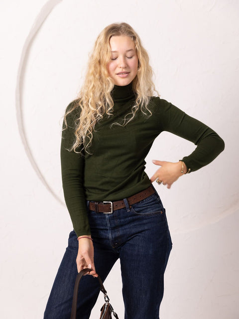 3. Woman holding TOKS VISOKS TOMMY leather bag in cognac, styled with green turtleneck and jeans