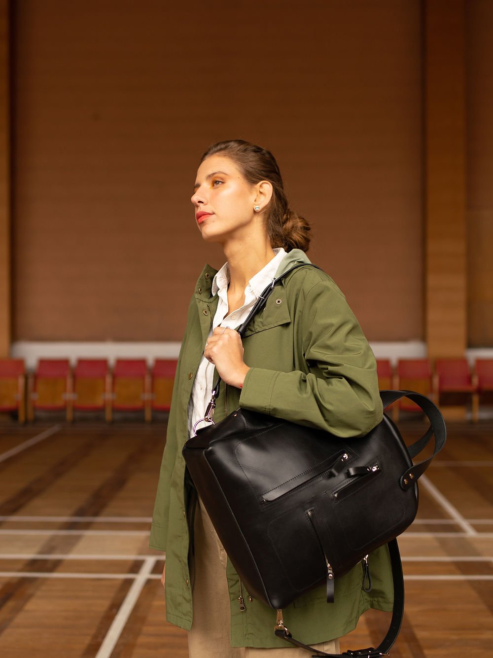 1. Woman holding TOKS VISOKS GORDON black leather backpack, showcasing front zipped pockets in lifestyle setting