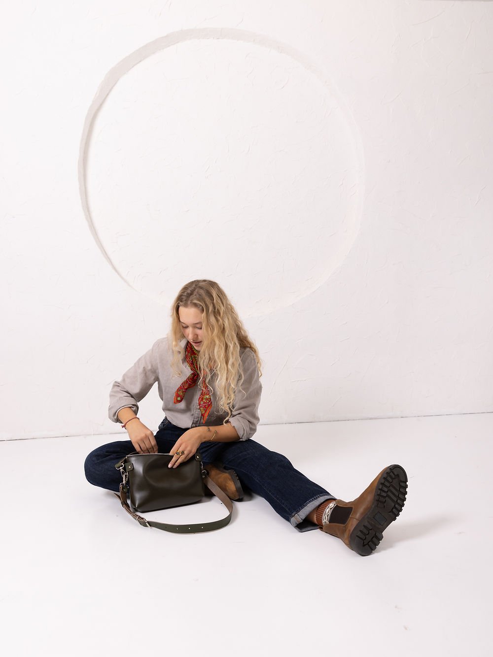 8. Lifestyle image of woman sitting with TOMMY leather bag in dirty green, showcasing casual styling