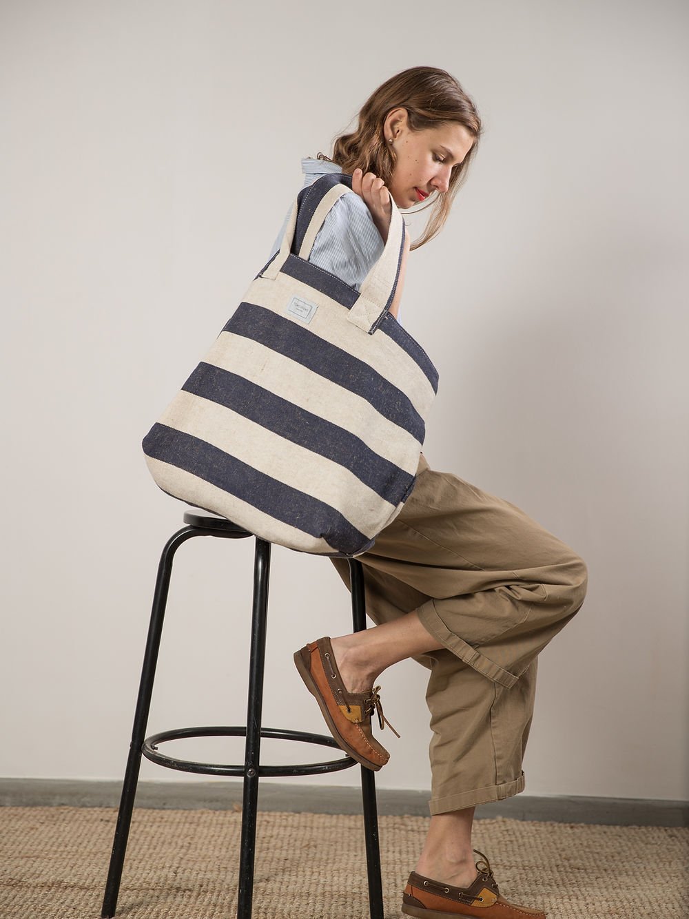 9. Woman sitting sideways with TOKS VISOKS oversized beach bag in reclaimed stripe canvas, studio setting