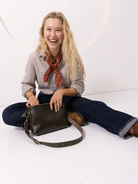 5. Lifestyle image of woman sitting with TOMMY leather bag in dirty green, showing casual styling