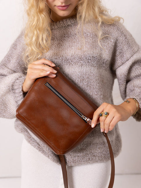 3. Close-up of woman holding TOKS VISOKS ARLO Purse in ginger, highlighting zipped back pocket and leather texture