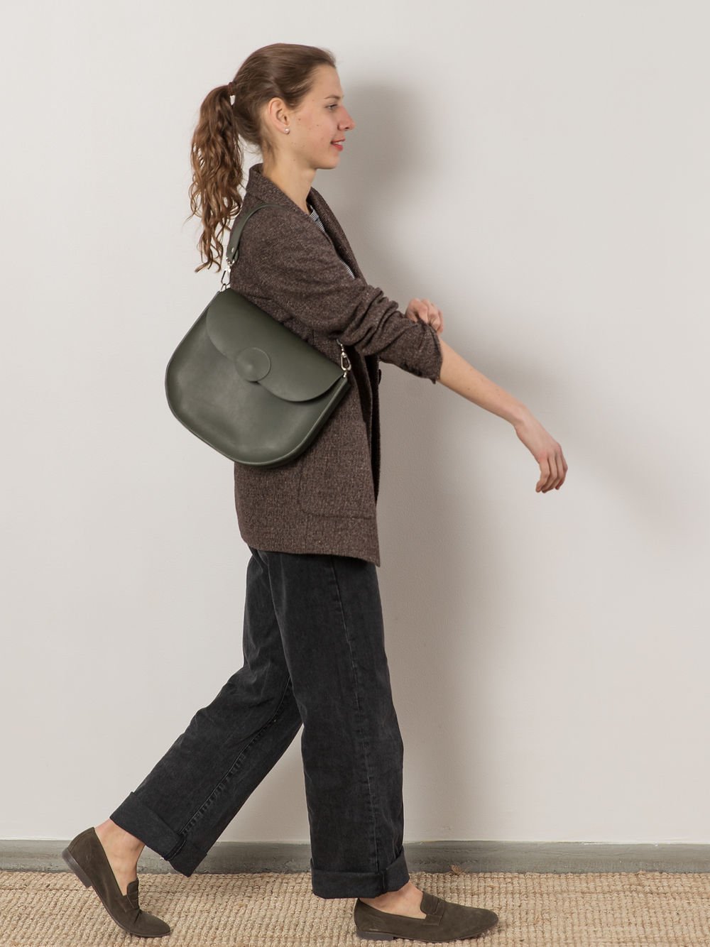 4. Woman walking with TOKS VISOKS FIONA Handbag in faded green, demonstrating hands-free carrying