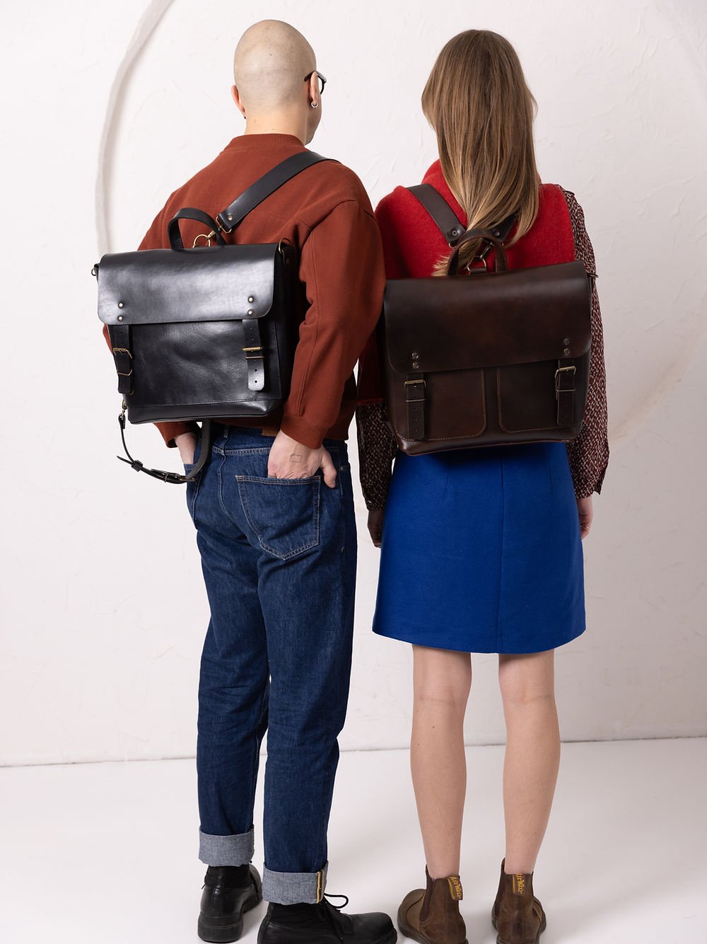 2. Male and female models wearing TOKS VISOKS BENJAMIN Backpack in dark chocolate leather, shown from the back