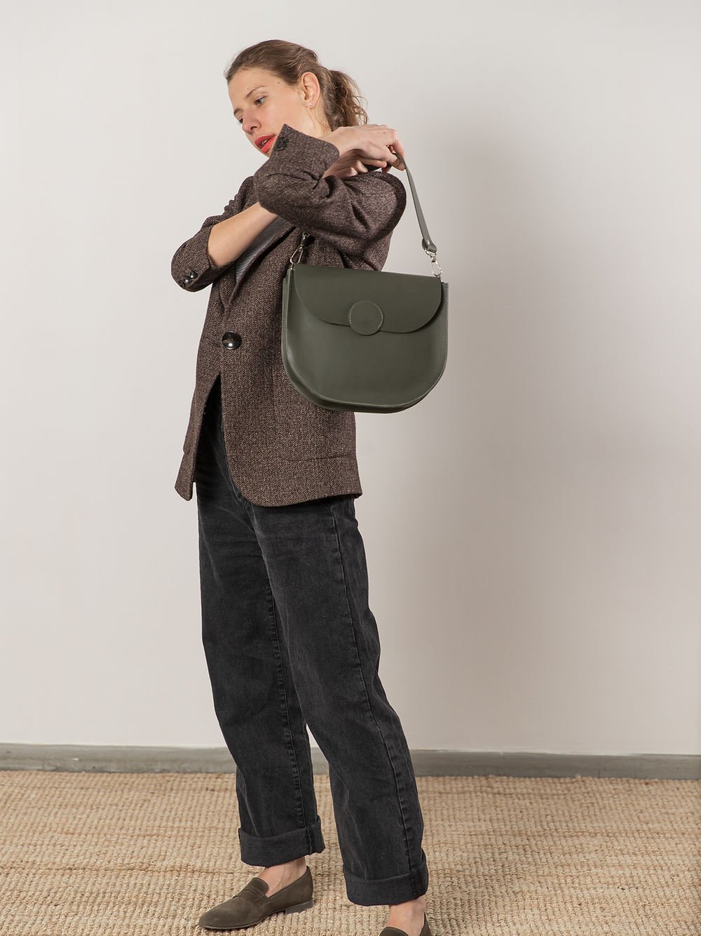 7. Woman holding TOKS VISOKS FIONA Handbag in faded green by handle, studio setting