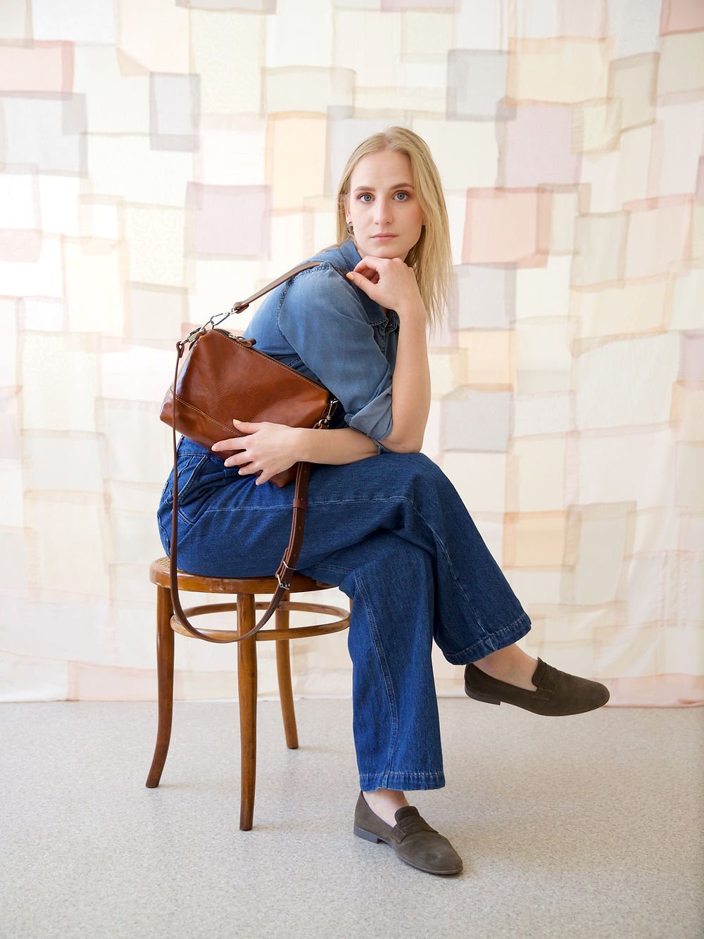 7. Woman seated with TOKS VISOKS ROBIN leather handbag in ginger brown, styled with denim attire