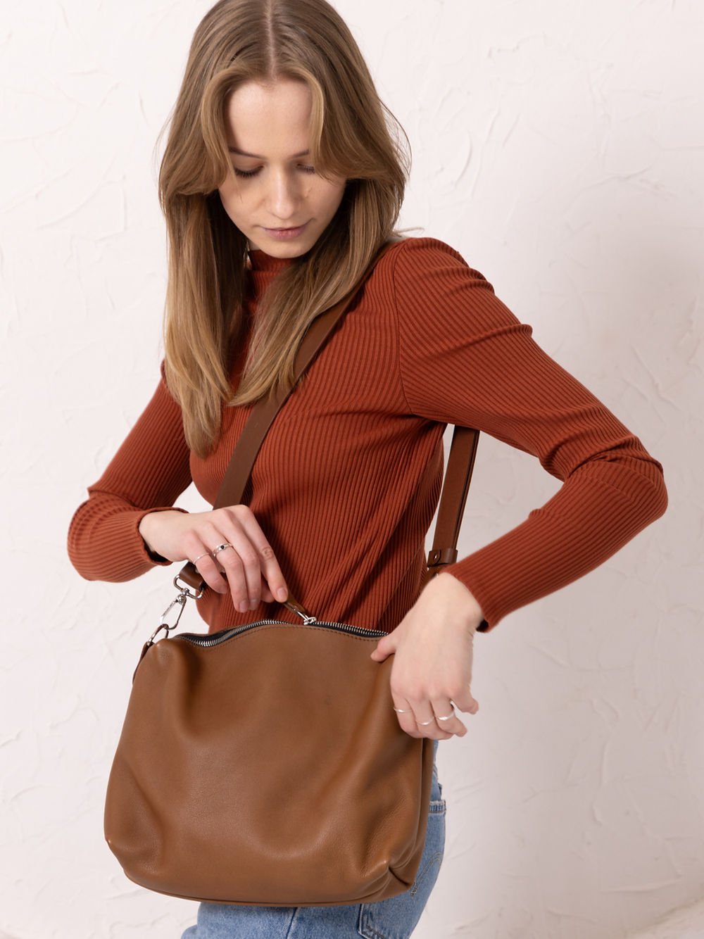 6. Woman opening TOKS VISOKS ROBIN leather handbag in camel brown, studio setting