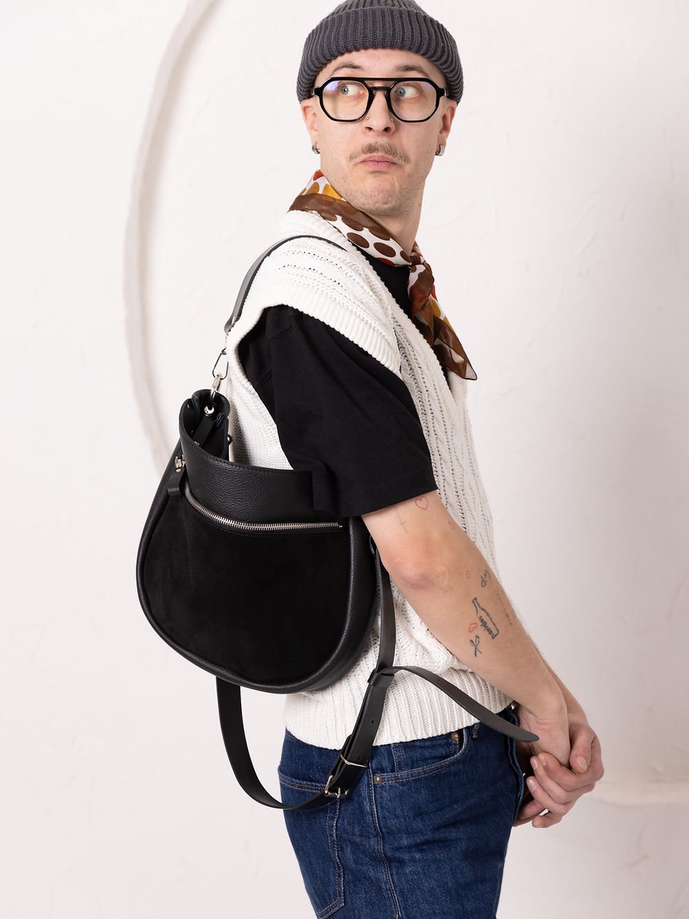 7. Unisex model holding TOKS VISOKS STELLA black leather handbag by the strap, styled with casual outfit in studio