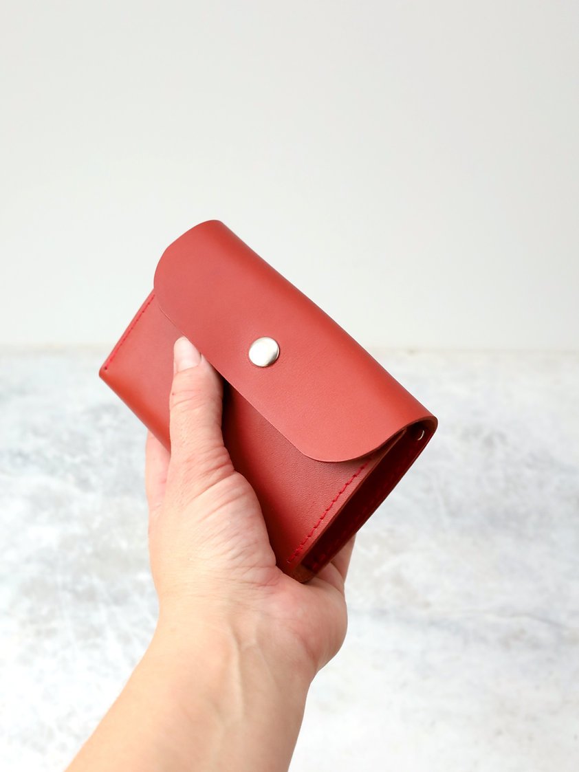 9. Hand holding closed TOKS VISOKS FRIDAY Wallet in faded red, emphasizing portability