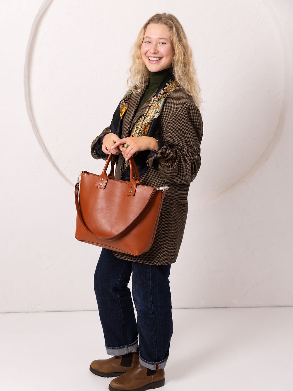 3. Full-body view of woman carrying TOKS VISOKS MIGLE leather handbag in ginger, paired with casual outfit