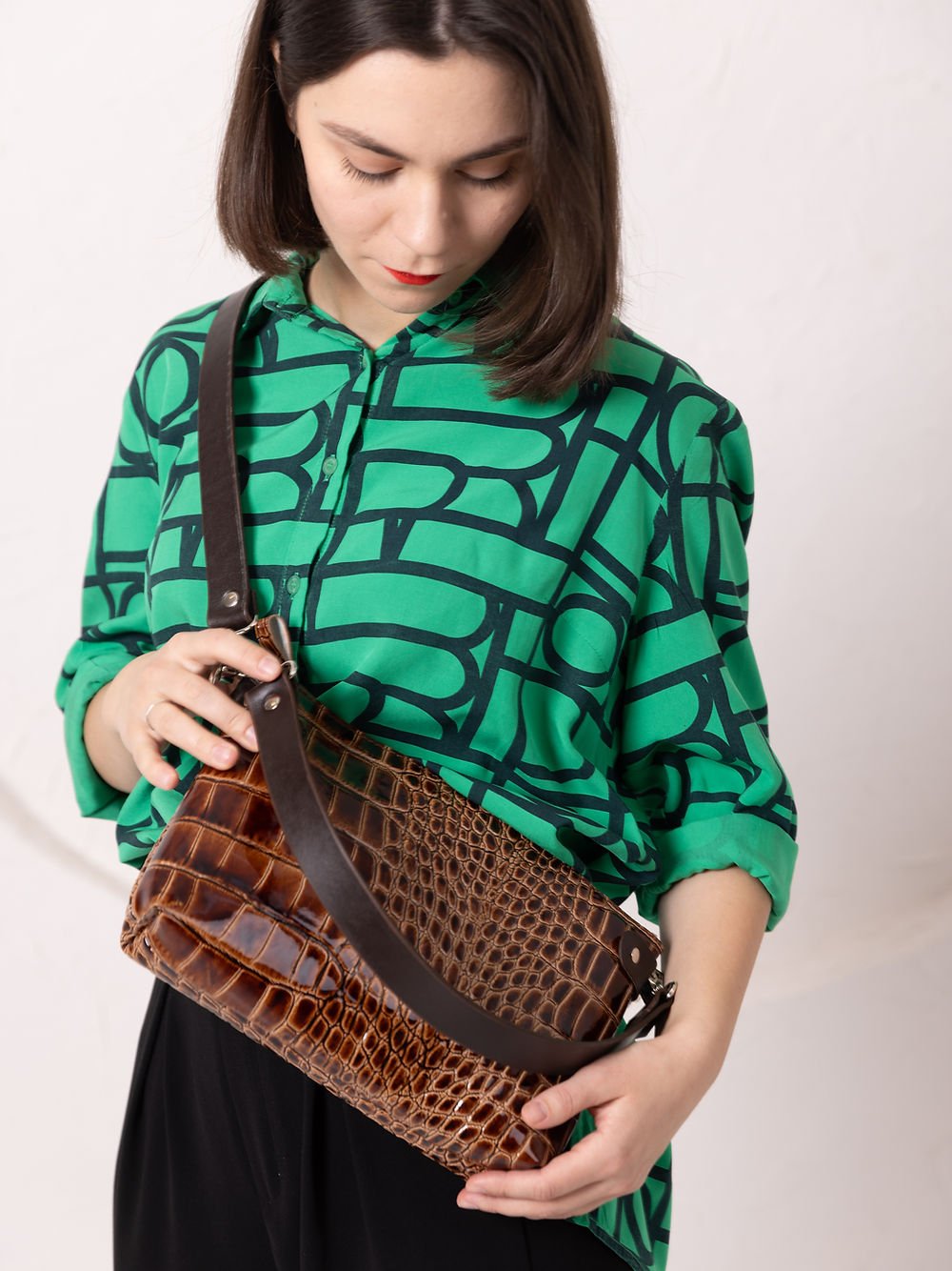 7. Woman showcasing TOKS VISOKS TOMMY leather bag with alligator pattern, styled with green shirt