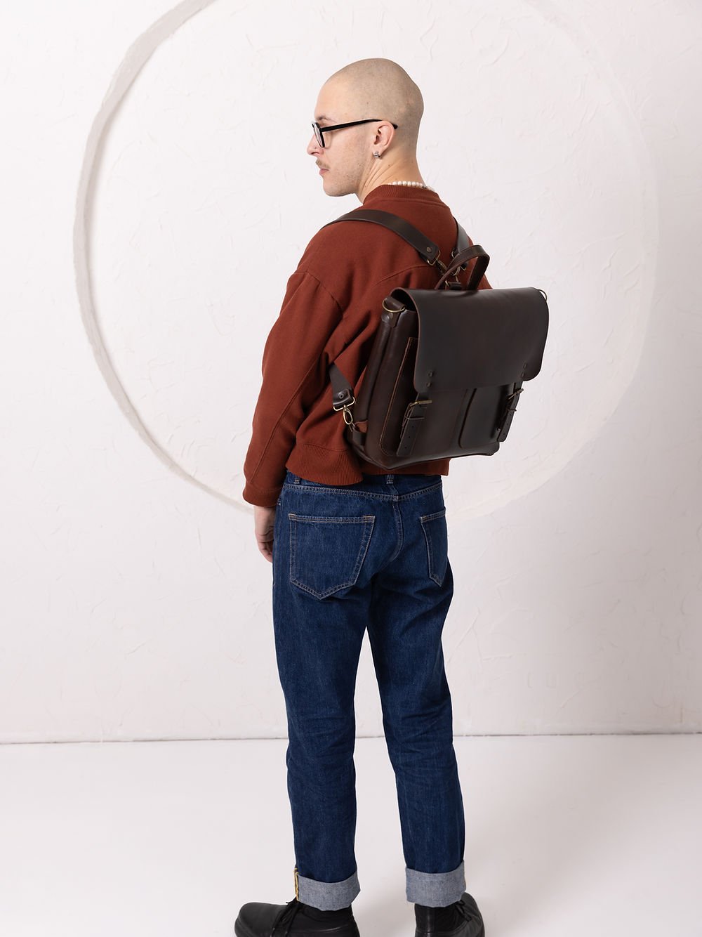 6. Male model adjusting TOKS VISOKS BENJAMIN Backpack in dark chocolate leather, focusing on side view