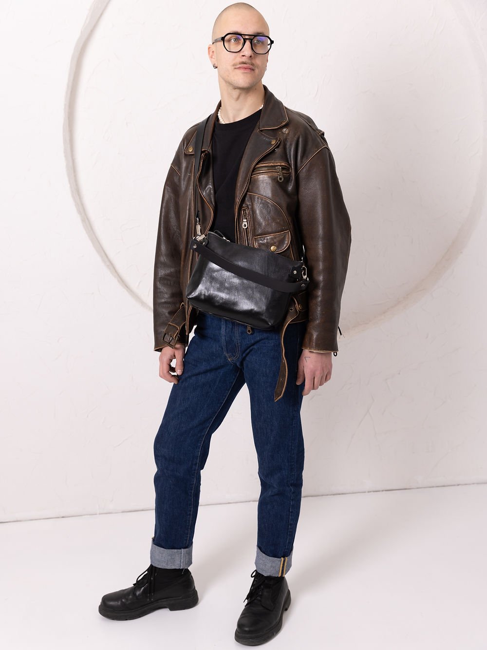 7. Unisex black TOMMY leather bag by TOKS VISOKS worn crossbody with leather jacket in studio setting