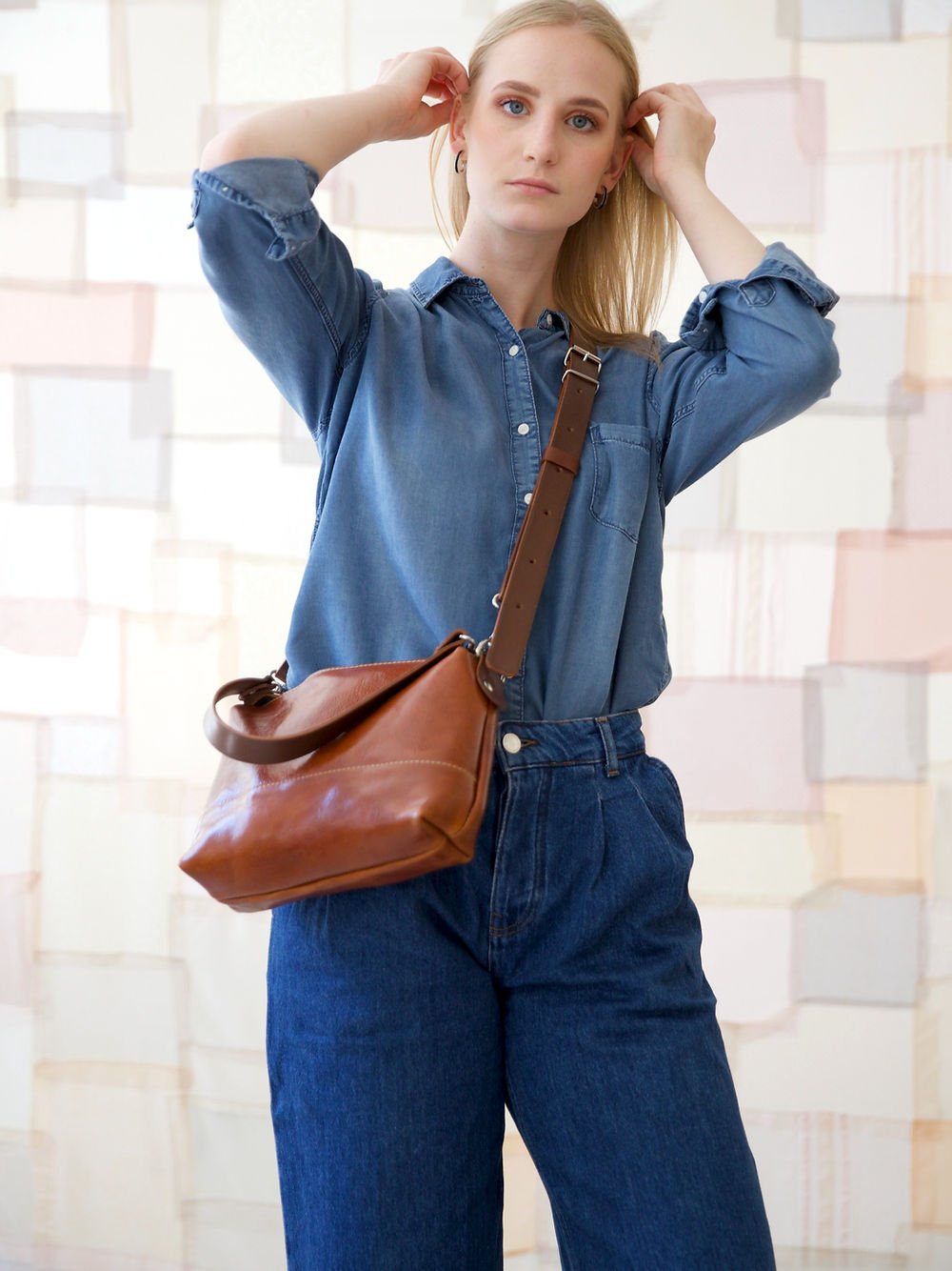 1. Woman wearing TOKS VISOKS ROBIN leather handbag in ginger brown, styled with denim shirt and jeans