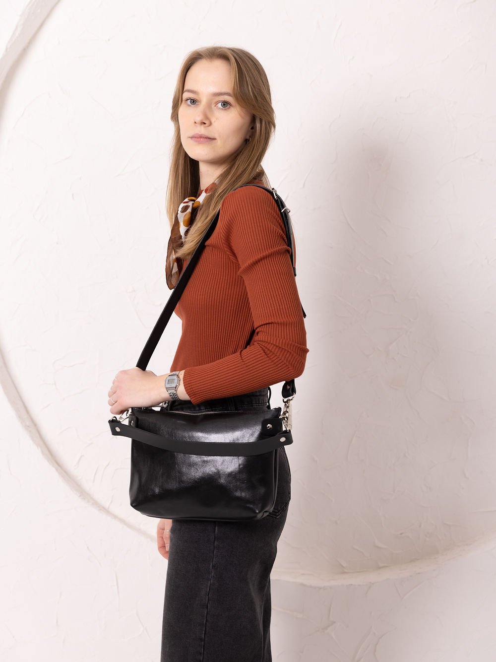 8. Women's black TOMMY leather bag by TOKS VISOKS worn on shoulder, side view in studio setting