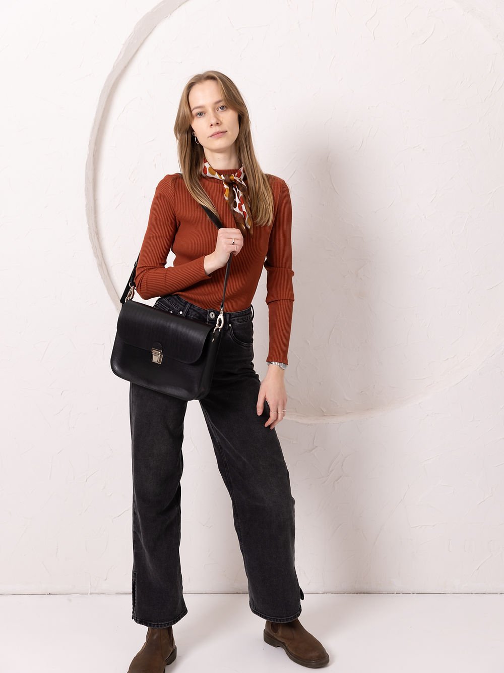 1. Woman wearing TOKS VISOKS ASTORIA black leather handbag with old-fashioned buckle in lifestyle setting