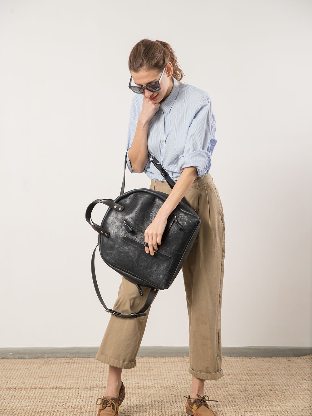 5. Woman holding TOKS VISOKS GORDON Backpack in dark denim, demonstrating front zipped pockets