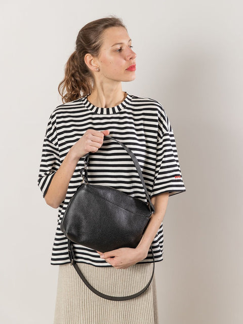 4. Woman showcasing TOKS VISOKS ROBIN black leather handbag with versatile carrying options