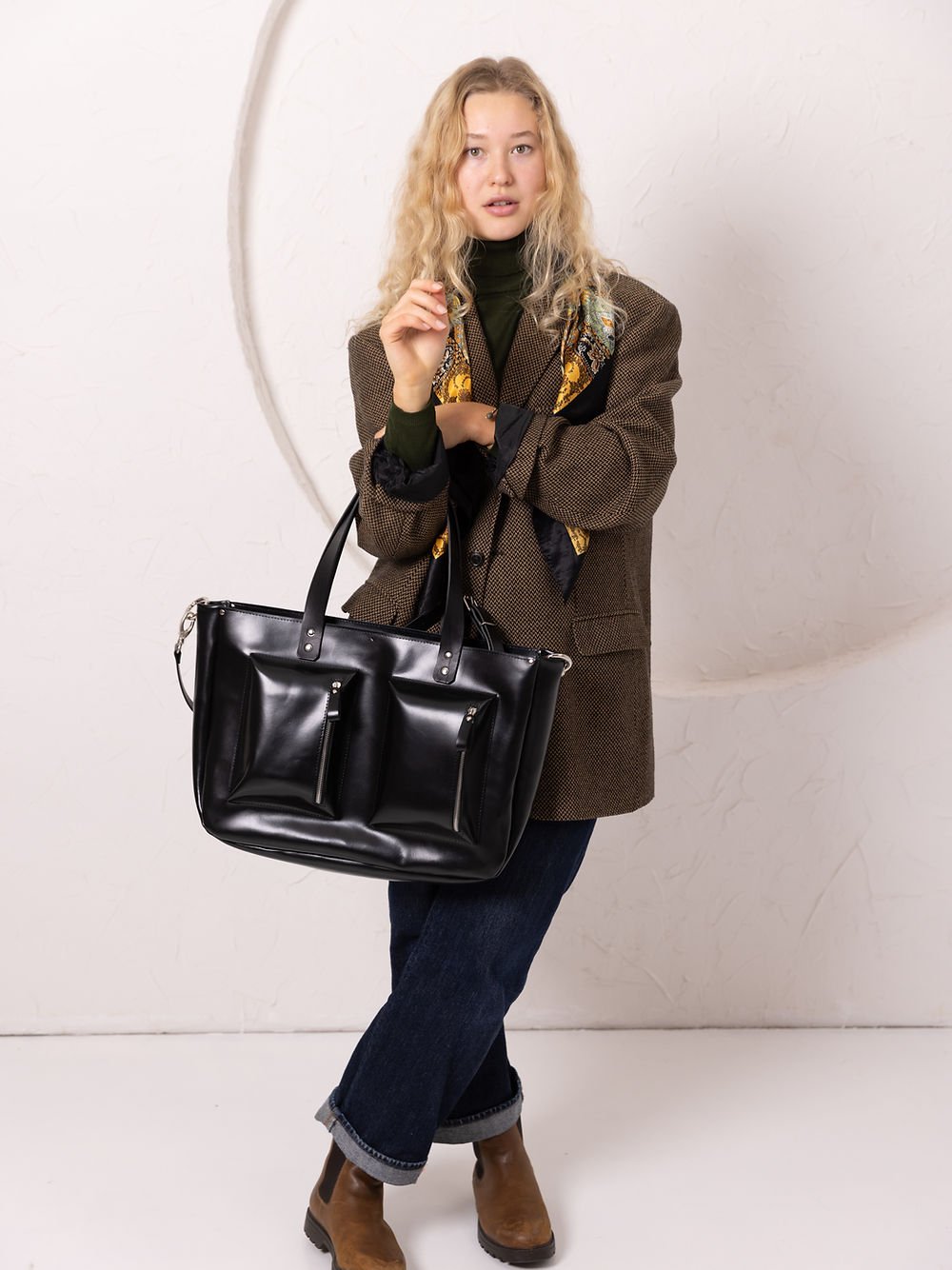 3. Women's black AMBER handbag by TOKS VISOKS, worn with a brown coat and jeans, shown in a studio setting