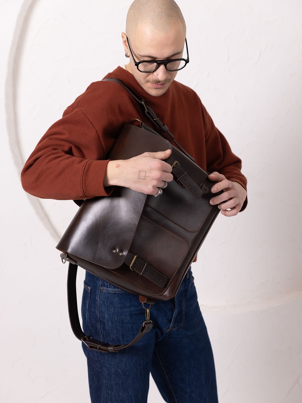 8. Male model holding TOKS VISOKS BENJAMIN Backpack in dark chocolate leather, showcasing versatile carrying options